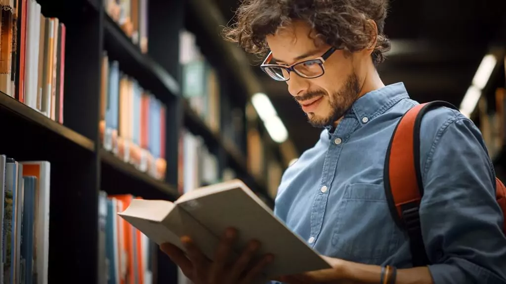 rapaz lendo livro em biblioteca