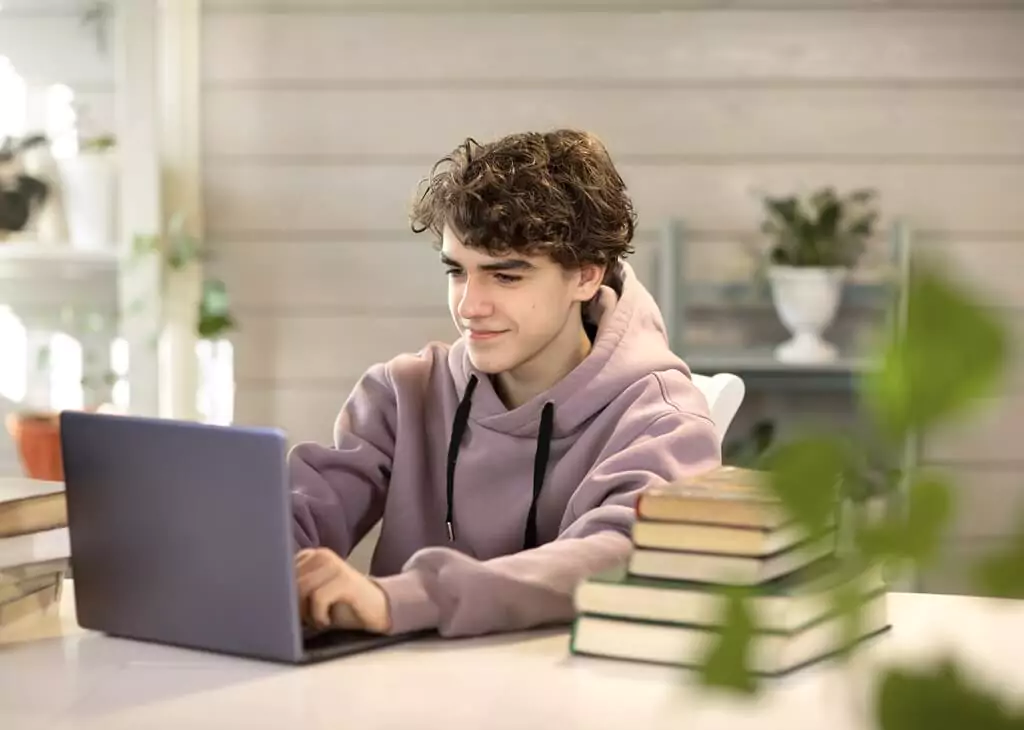 rapaz pesquisando em computador ao lado de pilha de livros