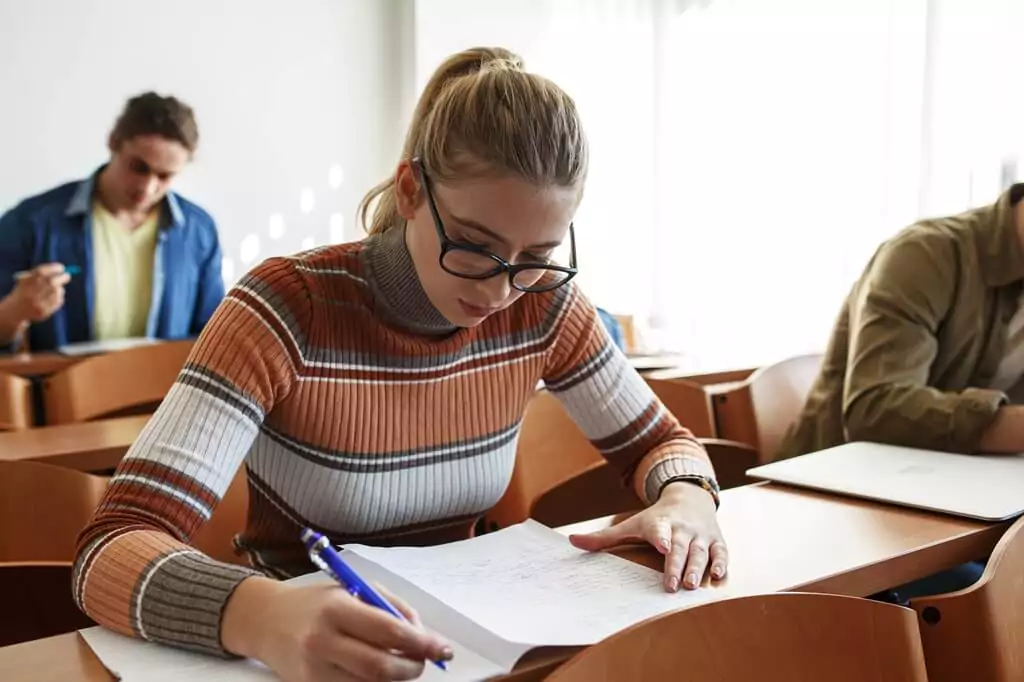 moça fazendo prova em sala de aula com outras pessoas