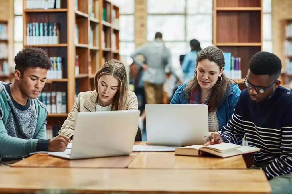 estudantes em biblioteca com computadores e livros