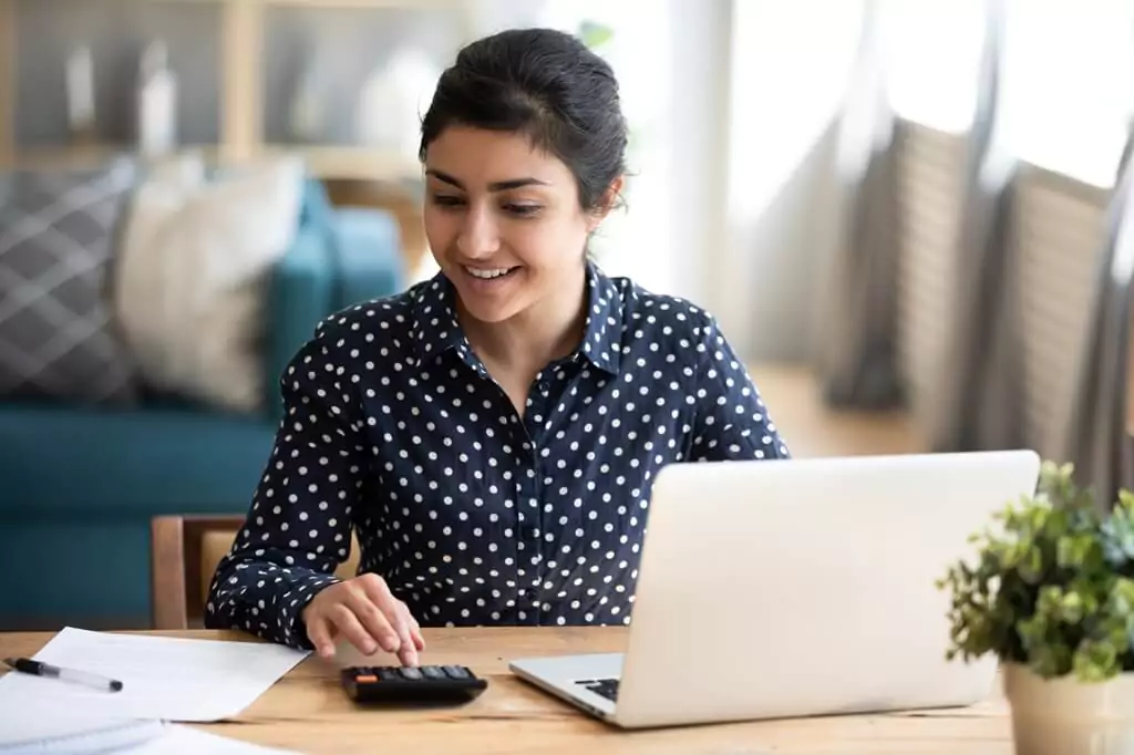 moça fazendo cálculos com calculadora ao lado de laptop