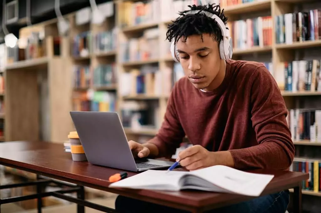 aluno em biblioteca estudando com livros e computador