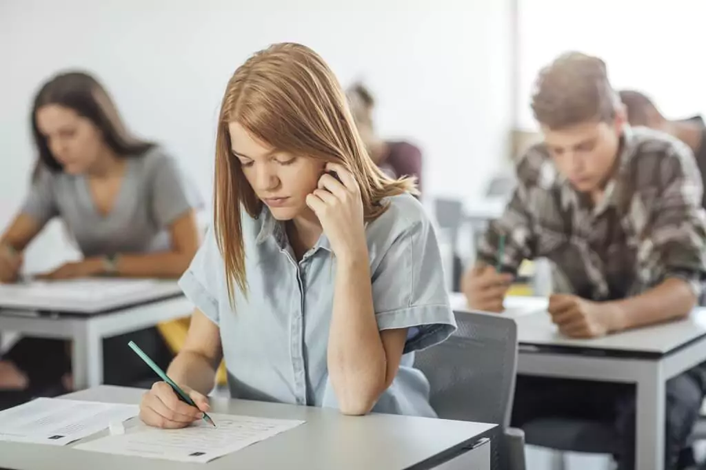 menina fazendo prova com outras pessoas em sala de aula