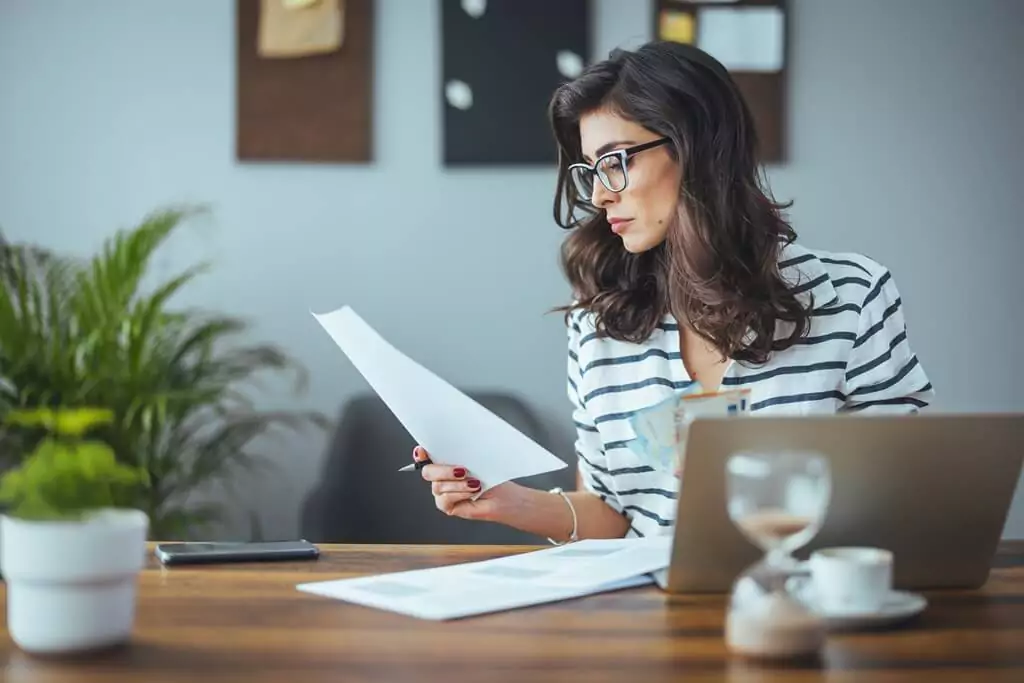 mulher analisando documento diante de computador