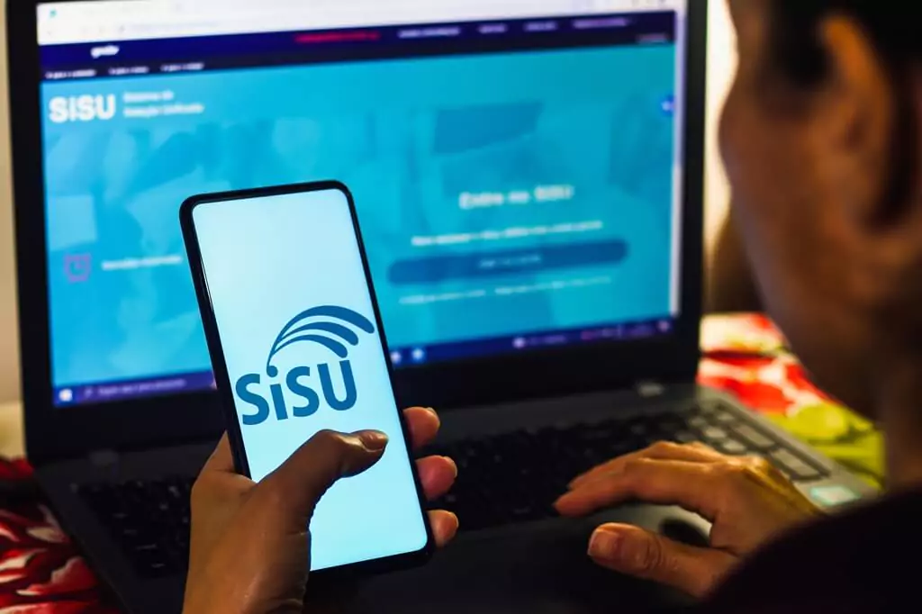 moça acessando celular com app do Sisu e mexendo em computador com site do Sisu