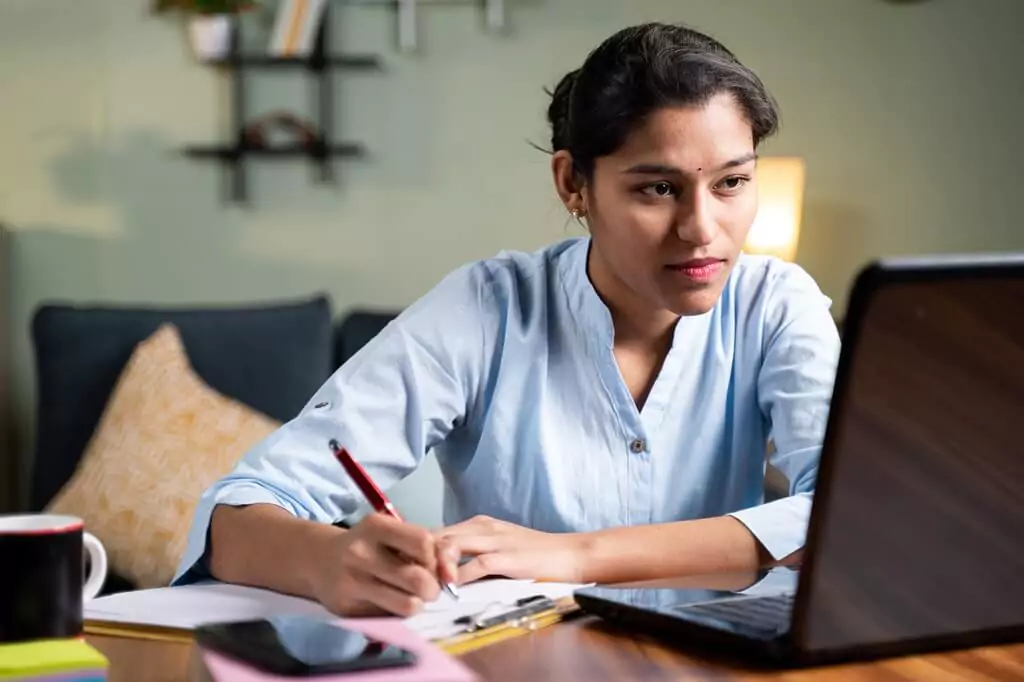 moça estudando com computador e fazendo anotações