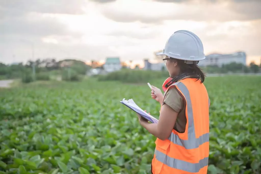 moça com prancheta e capacete em plantação