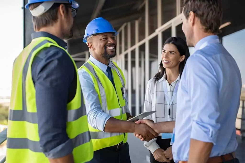 engenheiro apertando a mão de cliente com colegas ao redor