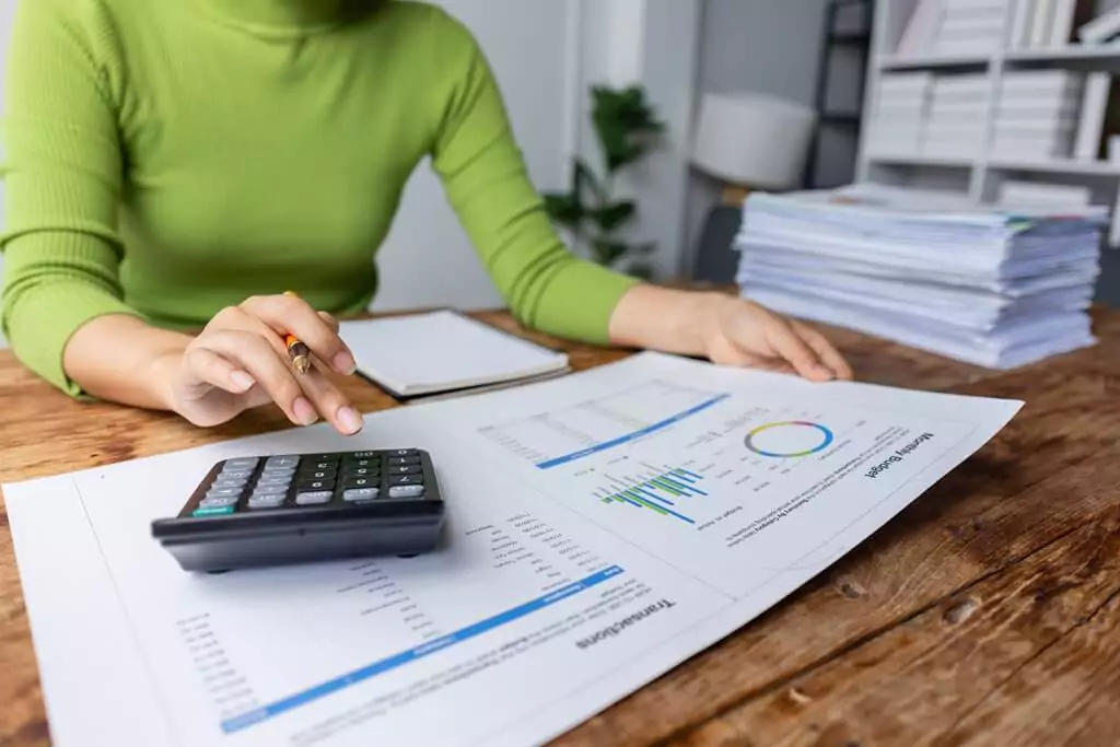 mulher fazendo contas com calculadora e analisando relatórios